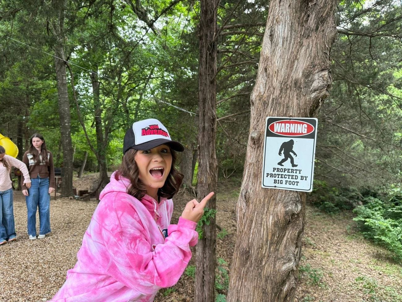 Annabella pointing at a Bigfoot warning sign nailed to a tree in one of Oregon's most Bigfoot-sighted forests